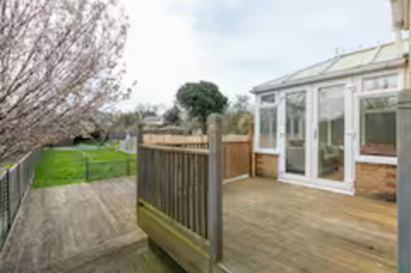 Garden with wooden deck, railings, green lawn, trees and conservatory extension