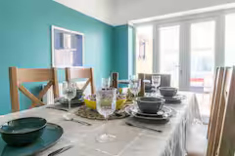 Bright dining room with turquoise walls, wooden chairs, set table with dishes and centerpiece