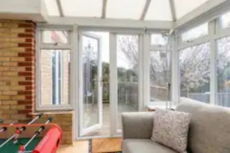 Bright conservatory with foosball table, grey sofa, large windows and glass doors overlooking garden