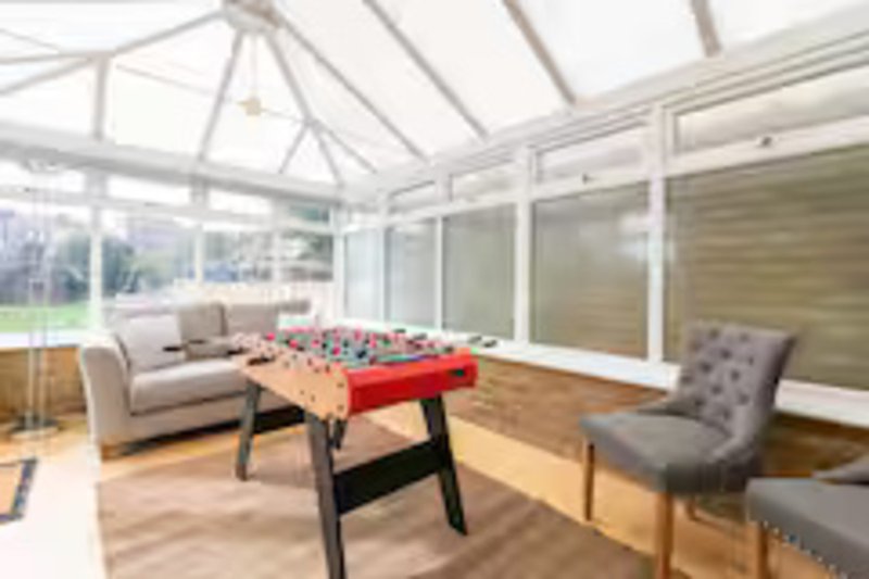 Bright conservatory with foosball table, gray sofa, armchair and wooden flooring