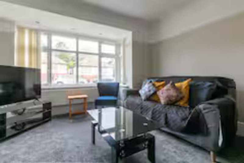 Modern living room with black sofa, TV, coffee table, and large window with street view