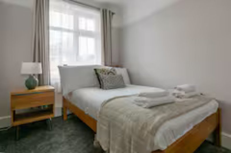Bright bedroom with two single beds, wooden nightstand, lamp, and large window with curtains