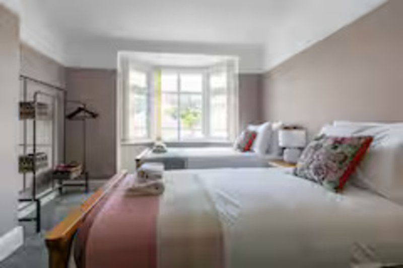 Bright modern bedroom with two double beds, large window, grey walls and contemporary furnishings