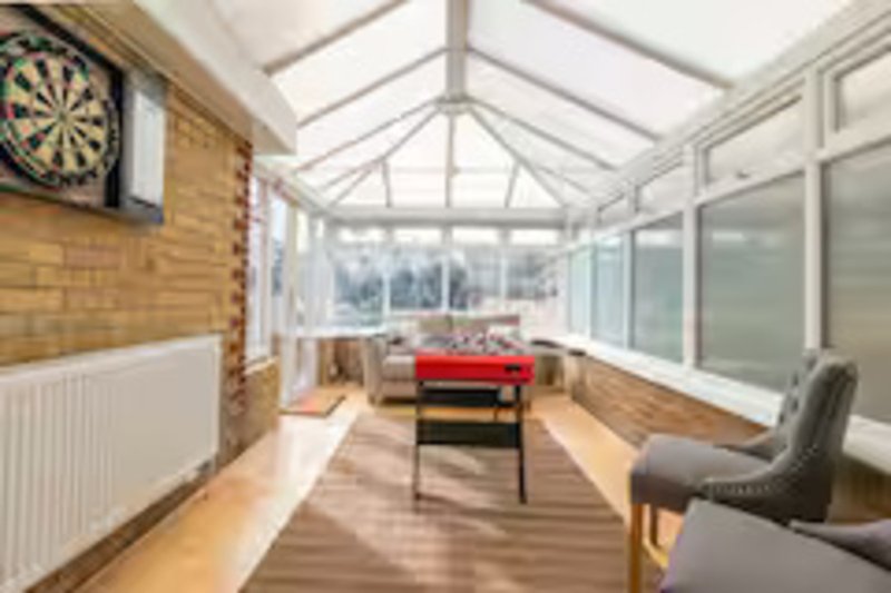 Bright conservatory with skylight, dartboard, red table, chairs and garden views