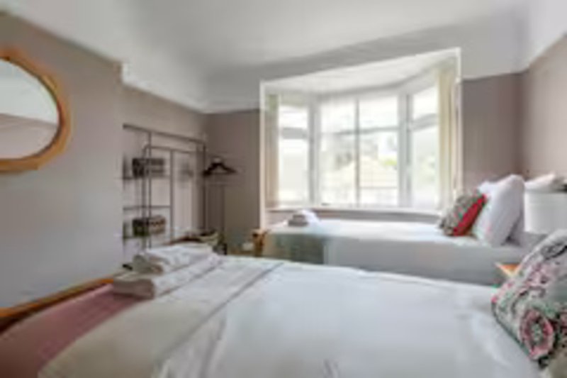 Bright bedroom with two beds, bay window, round mirror and neutral decor