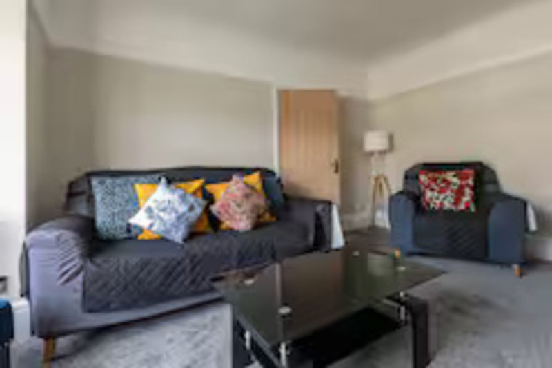 Living room with dark sofa, colorful cushions, armchair, coffee table and lamp