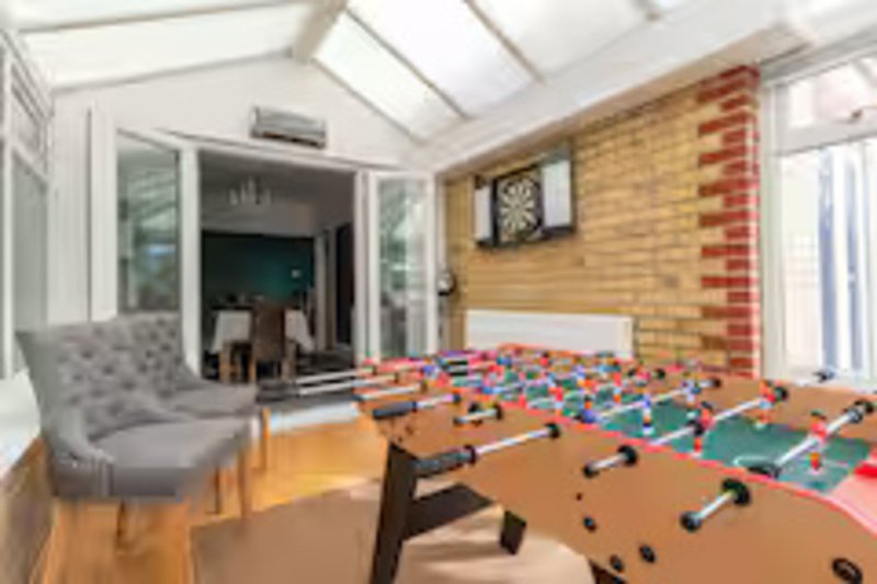 Modern conservatory with foosball table, gray armchair, and glass doors to kitchen