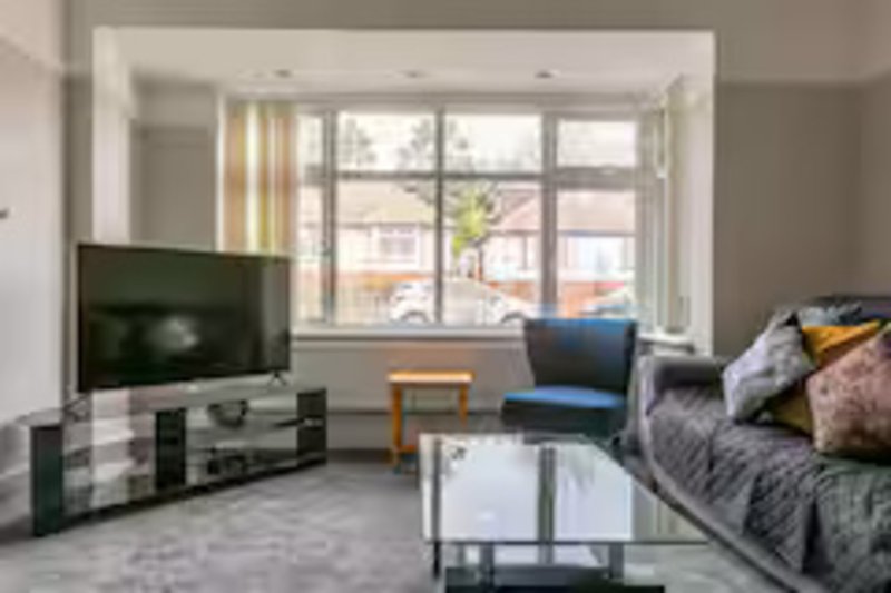 Bright living room with TV, sofa with cushions, armchair, coffee table and bay windows