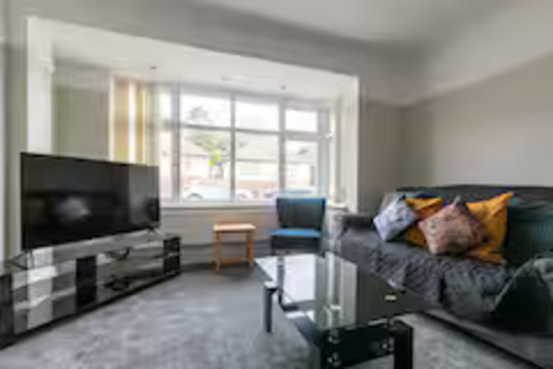 Bright living room with TV, sofa, armchair, coffee table and large windows