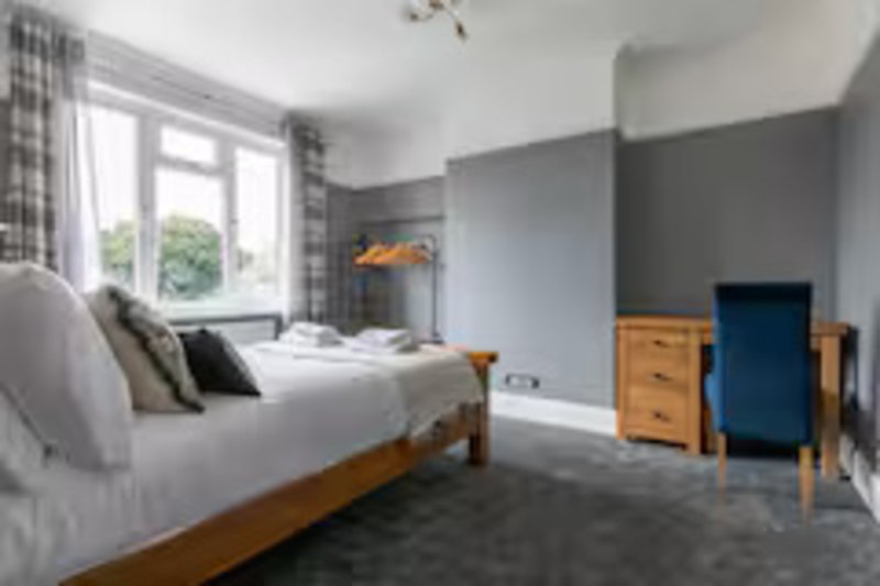 Bedroom with wooden bed, grey walls, blue door, chest of drawers and large window