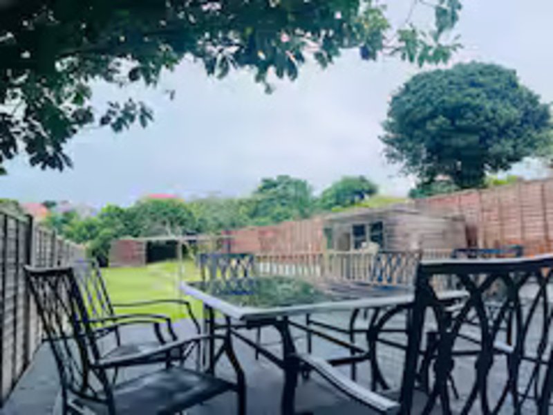Brick property exterior with patio seating area overlooking green lawn and countryside