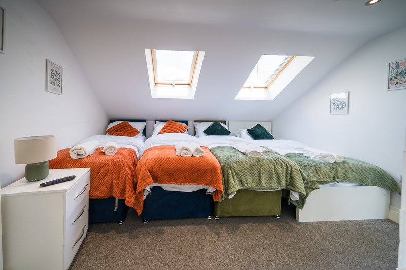 Attic bedroom with two single beds, orange and green bedding, skylights and white walls