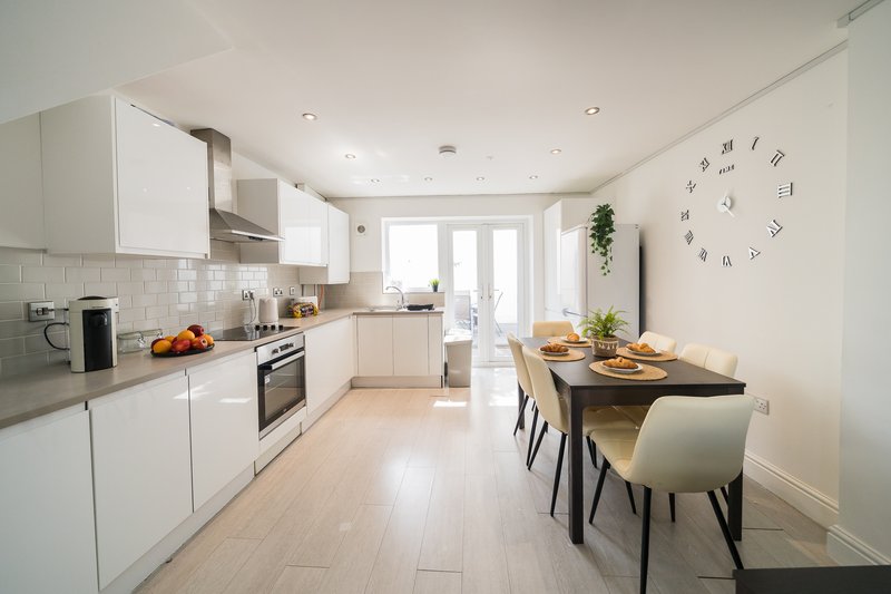 Modern white kitchen with dining table, appliances, and natural light from patio doors