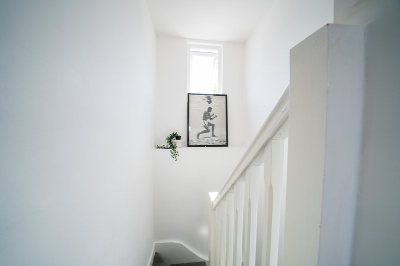 Bright stairwell with white walls, railing, framed artwork and small plant