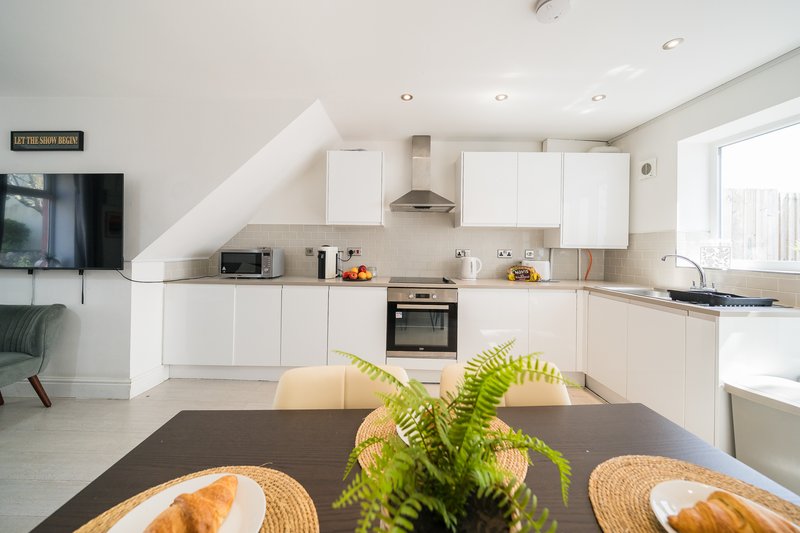 Modern kitchen with white cabinetry, dining table with place settings and potted plant