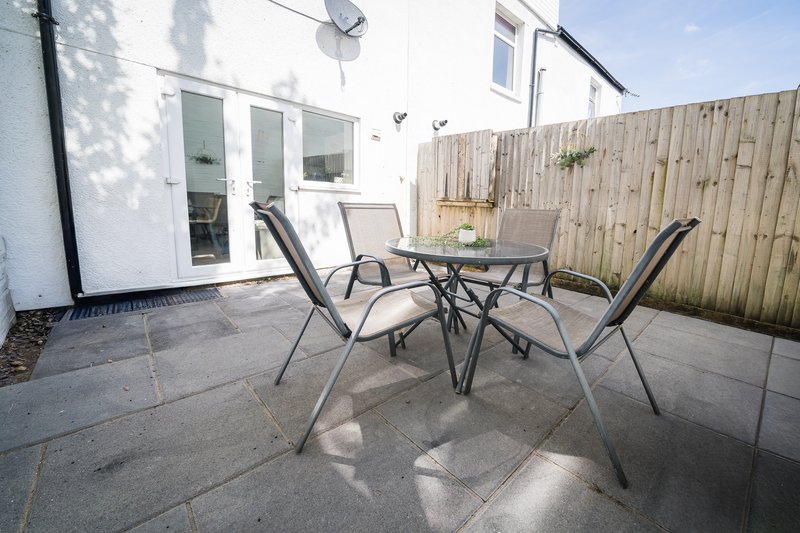 Modern patio with dining table, chairs, and wooden fence bordering property