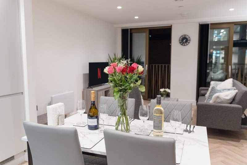 Open-plan living and dining area with white table, grey chairs, fresh flowers, and modern furnishings