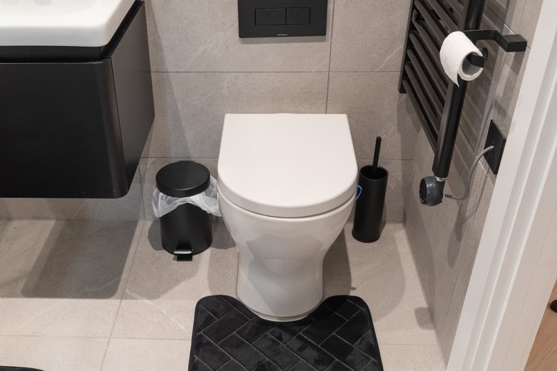 Modern bathroom with white toilet, black accessories, tiled floor and heated towel rail
