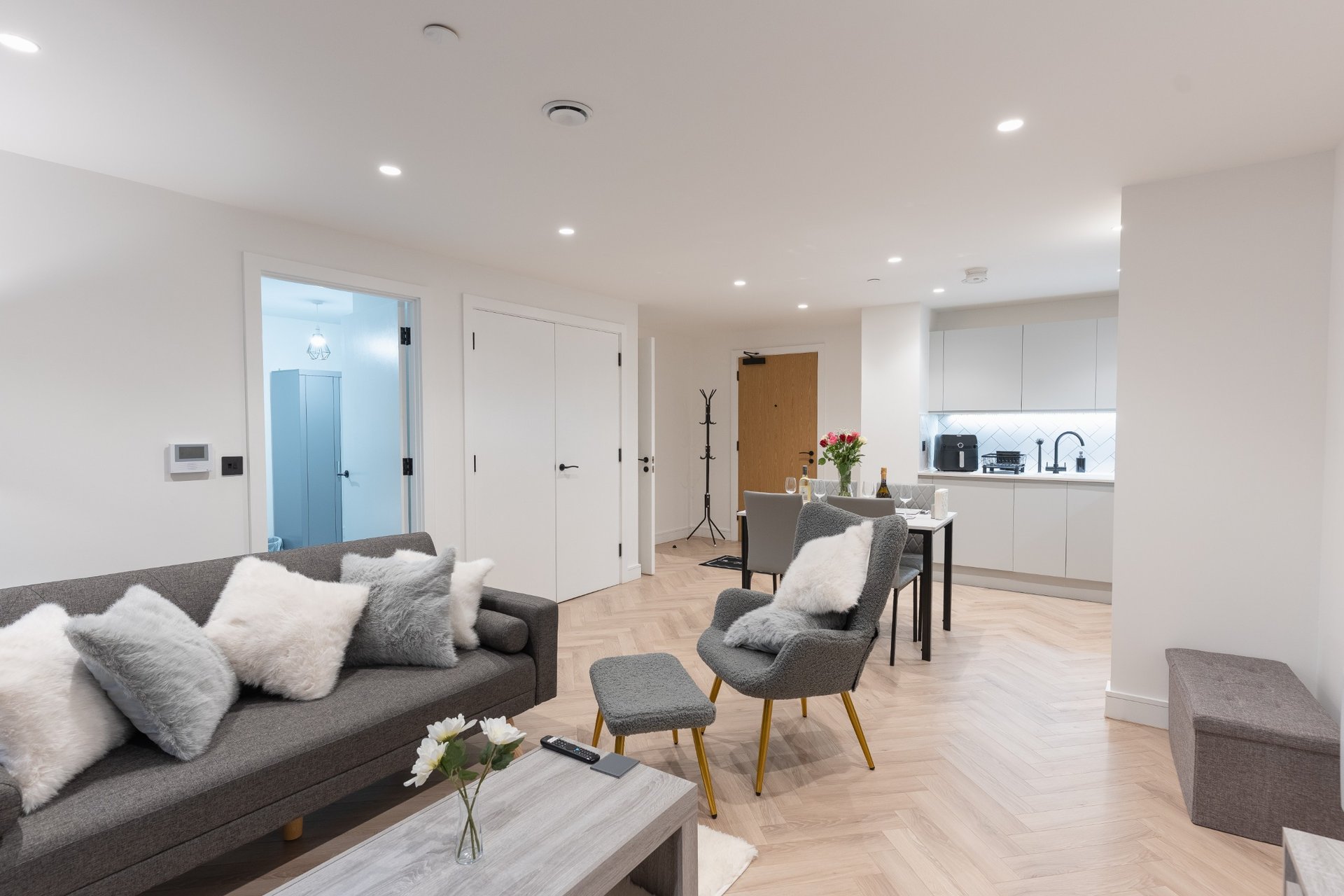 Modern open-plan living area with grey sofa, armchair, wooden flooring and kitchen beyond