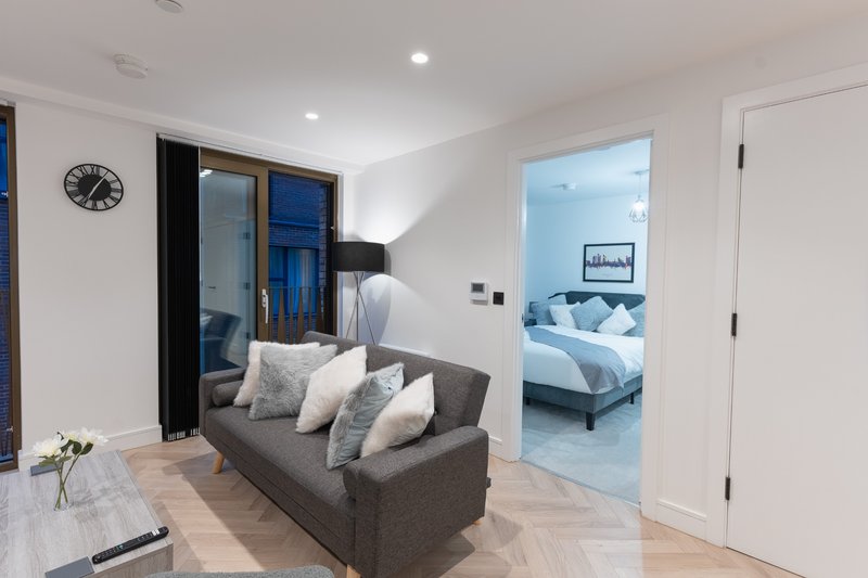 Modern living room with grey sofa, wall clock, glass sliding doors and view to bedroom