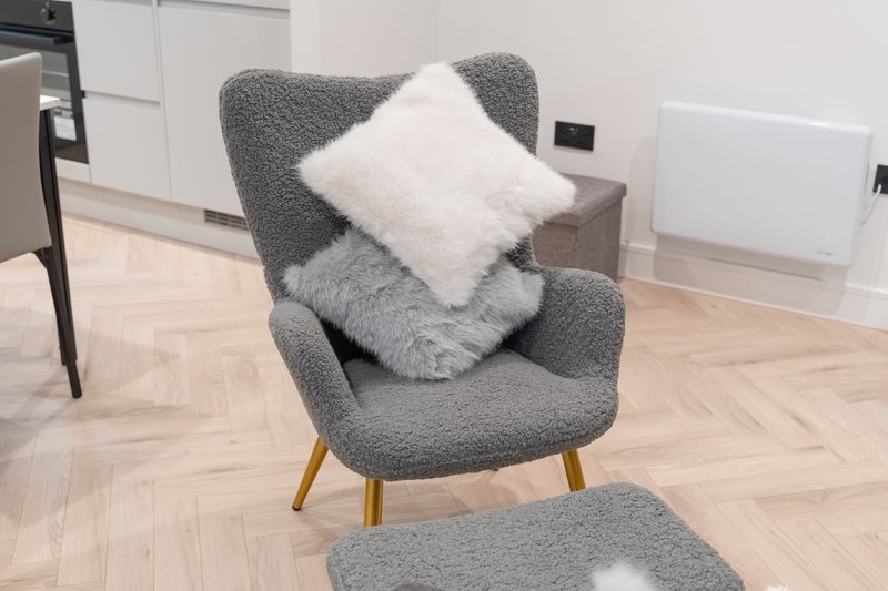 Gray upholstered armchair with white cushion and wooden legs on herringbone wood floor