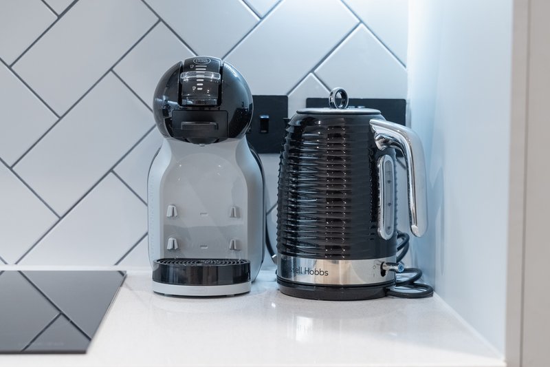Kitchen counter with white kettle and black coffee machine against blue subway tile backsplash