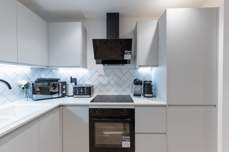 Modern white kitchen with black range hood, built-in oven, herringbone backsplash and appliances