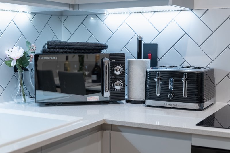 Modern kitchen counter with white herringbone tile backsplash, microwave, toaster, and decorative white flower vase