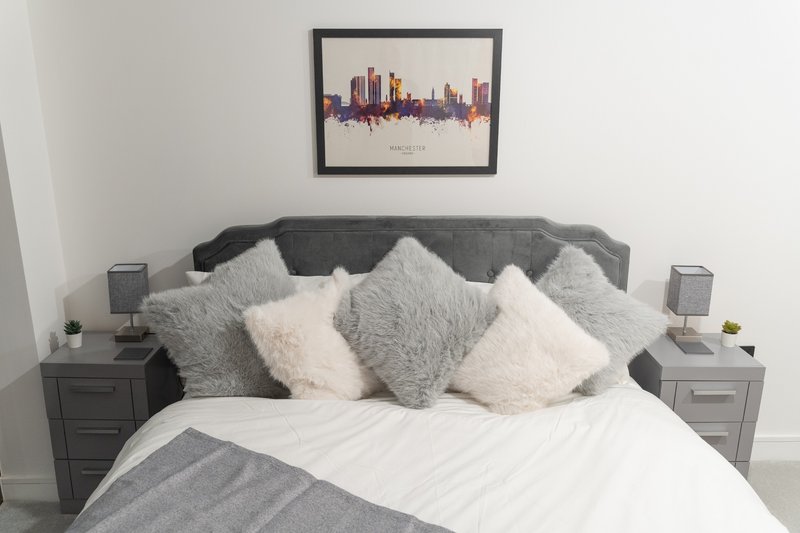Modern bedroom with grey upholstered bed, white and grey cushions, bedside tables and skyline artwork