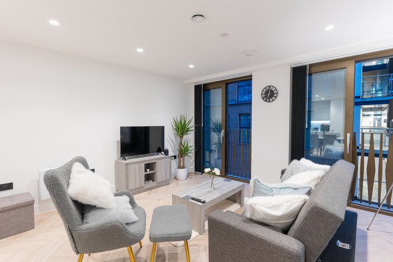 Modern living room with grey armchairs, TV, coffee table and blue-framed doors to balcony