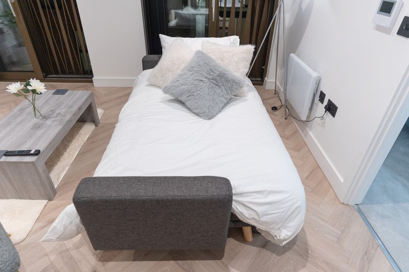 Modern bedroom with single bed, grey cushions, wooden floor and window with curtains