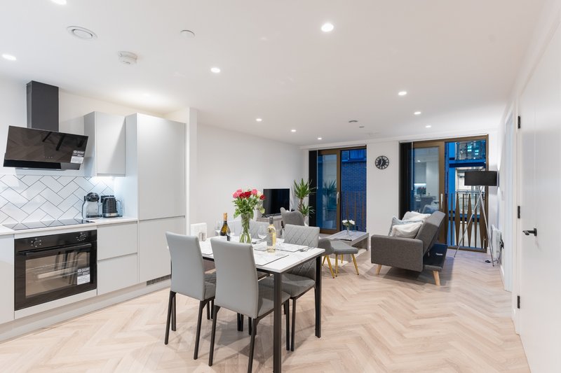 Modern open-plan kitchen-diner with white cabinetry, dining table, and lounge area visible