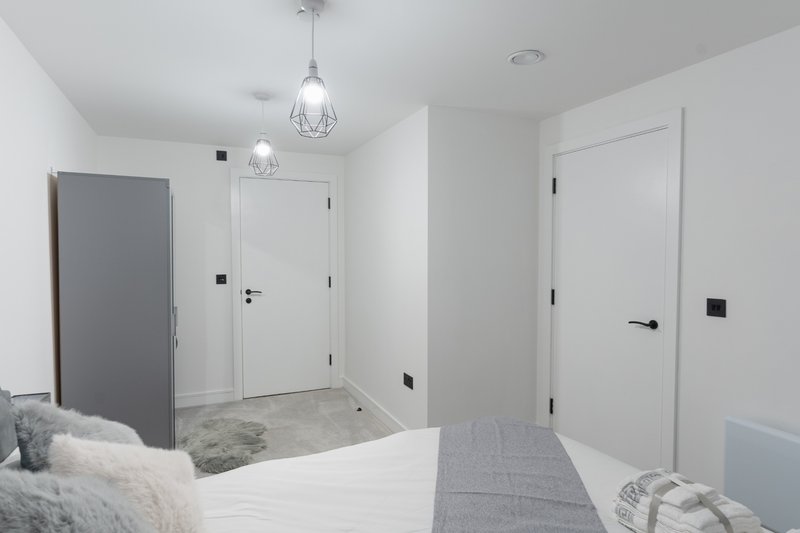 Modern bedroom with double bed, pendant lights, white doors and grey carpet hallway