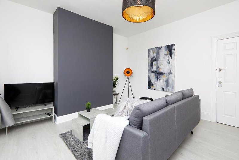 Modern living room with grey sofa, TV, dark accent wall, and artwork