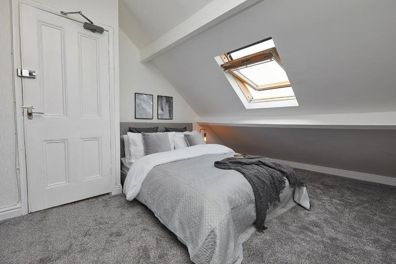 Modern attic bedroom with double bed, grey carpet, skylight window and white door