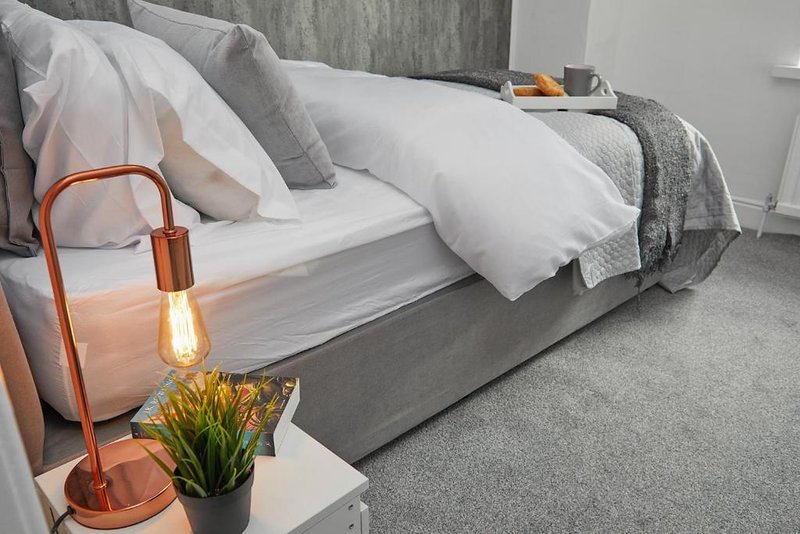 Modern bedroom with grey bed, white pillows, copper bedside lamp and yellow flowers