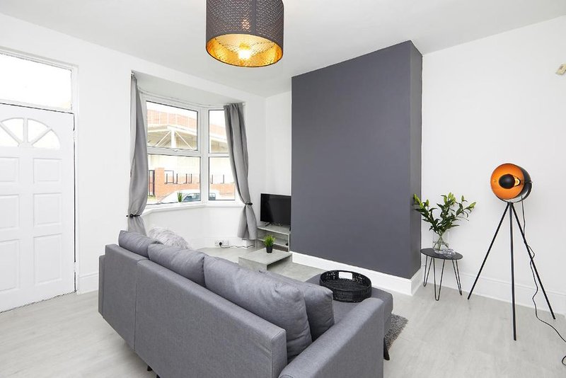 Modern living room with gray sofa, tripod lamp, TV stand and feature wall