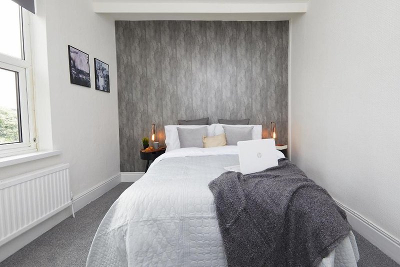 Modern bedroom with double bed, grey headboard wall, white bedding and throw blanket
