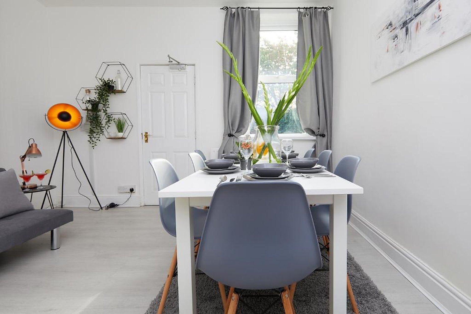 Modern dining room with white table, grey chairs, green plants in vase, and floor lamp