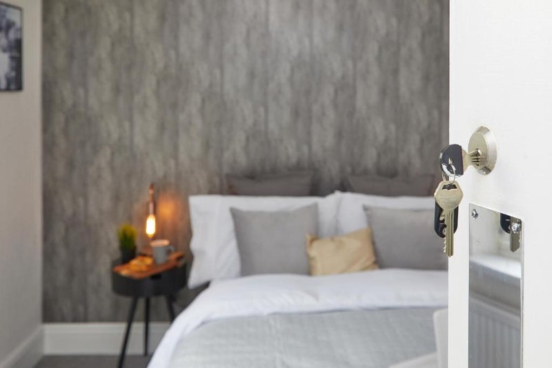 Modern bedroom with gray upholstered headboard, white bedding, side table with candle, and wall-mounted hooks