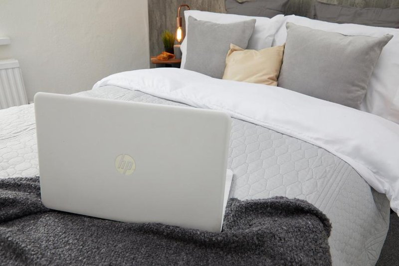 Bedroom with white laptop on grey throw, grey and cream pillows on bed