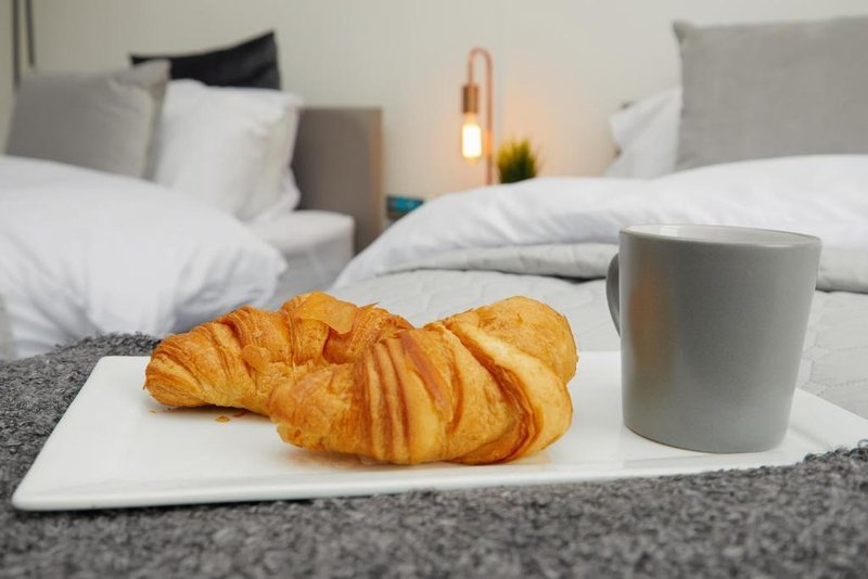 Modern bedroom with croissant and mug on bed, pillows and bedside lamp