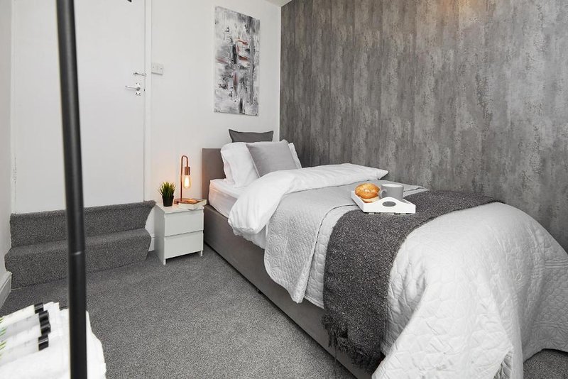 Modern bedroom with grey accent wall, single bed, white bedding, and minimalist furnishings