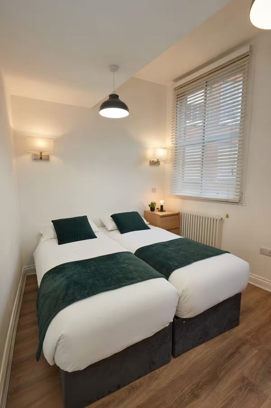 Bright bedroom with two single beds, white and dark green bedding, pendant light and wall sconces
