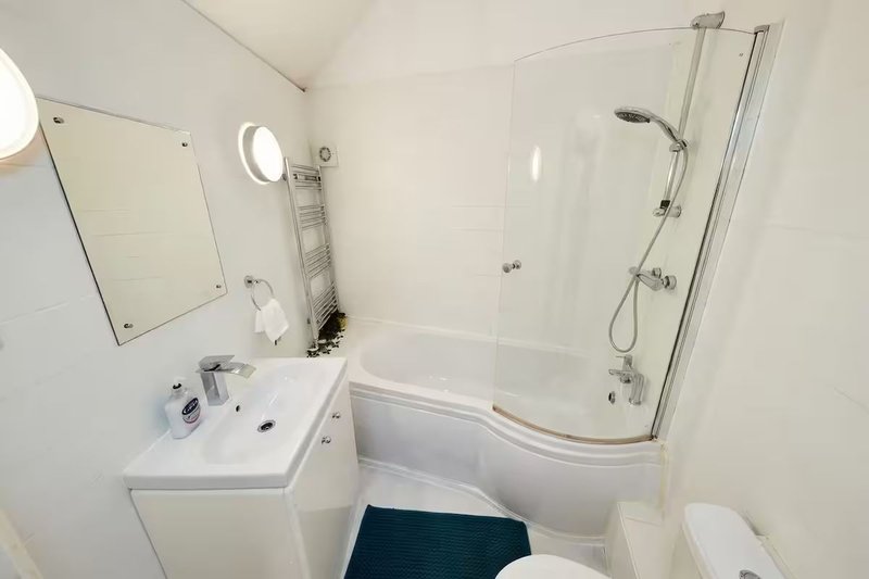 Modern bathroom with corner shower enclosure, white sink vanity, mirror and heated towel rail