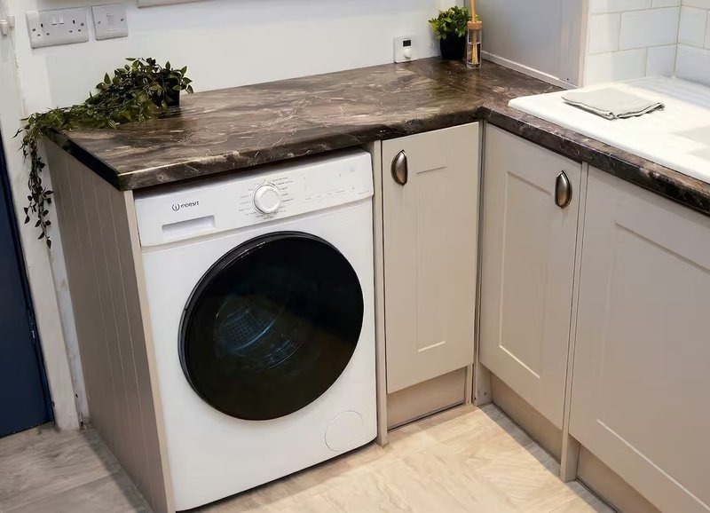 Kitchen with integrated washing machine, cream cabinetry, dark countertop and potted plant