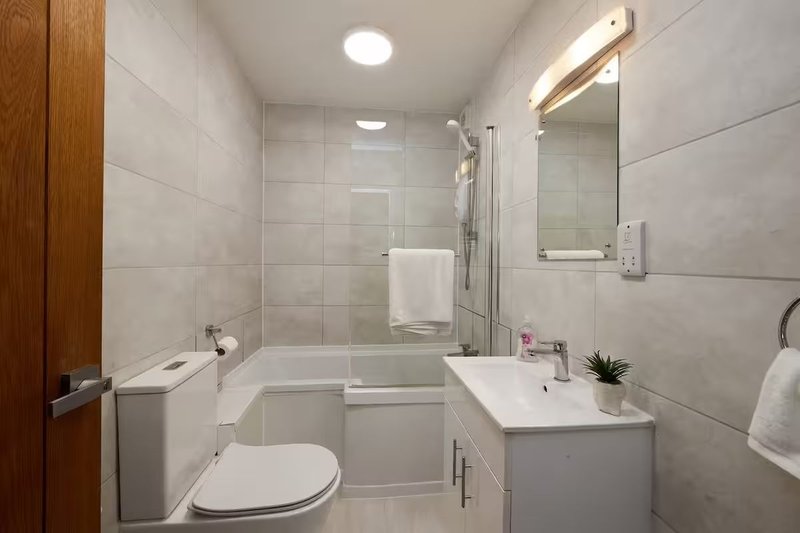 Clean modern bathroom with toilet, bathtub, sink vanity and mirror lighting
