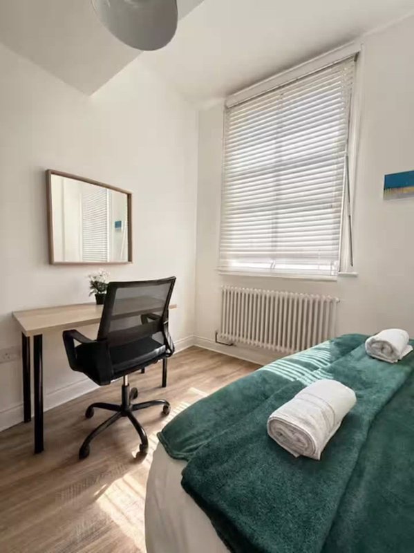Bright bedroom with double bed, desk, office chair and window with blinds