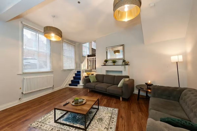Bright open-plan living room with wooden floor, grey sofas, wooden coffee table and pendant lights