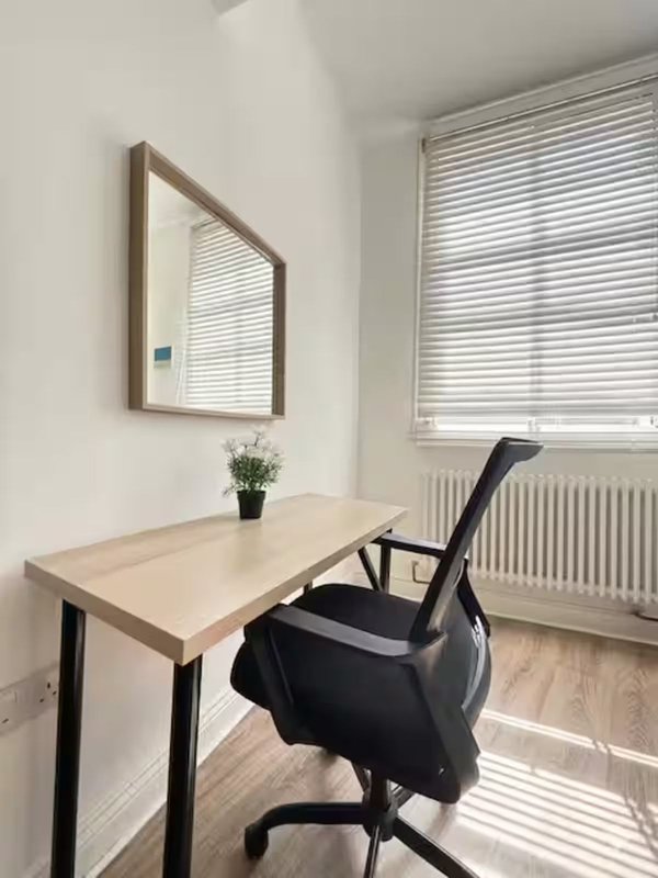 Minimalist home office with light wood desk, black office chair, and wall mirror